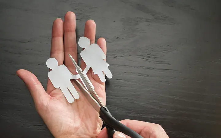 Mão segurando figuras de papel de um casal, separadas por uma tesoura